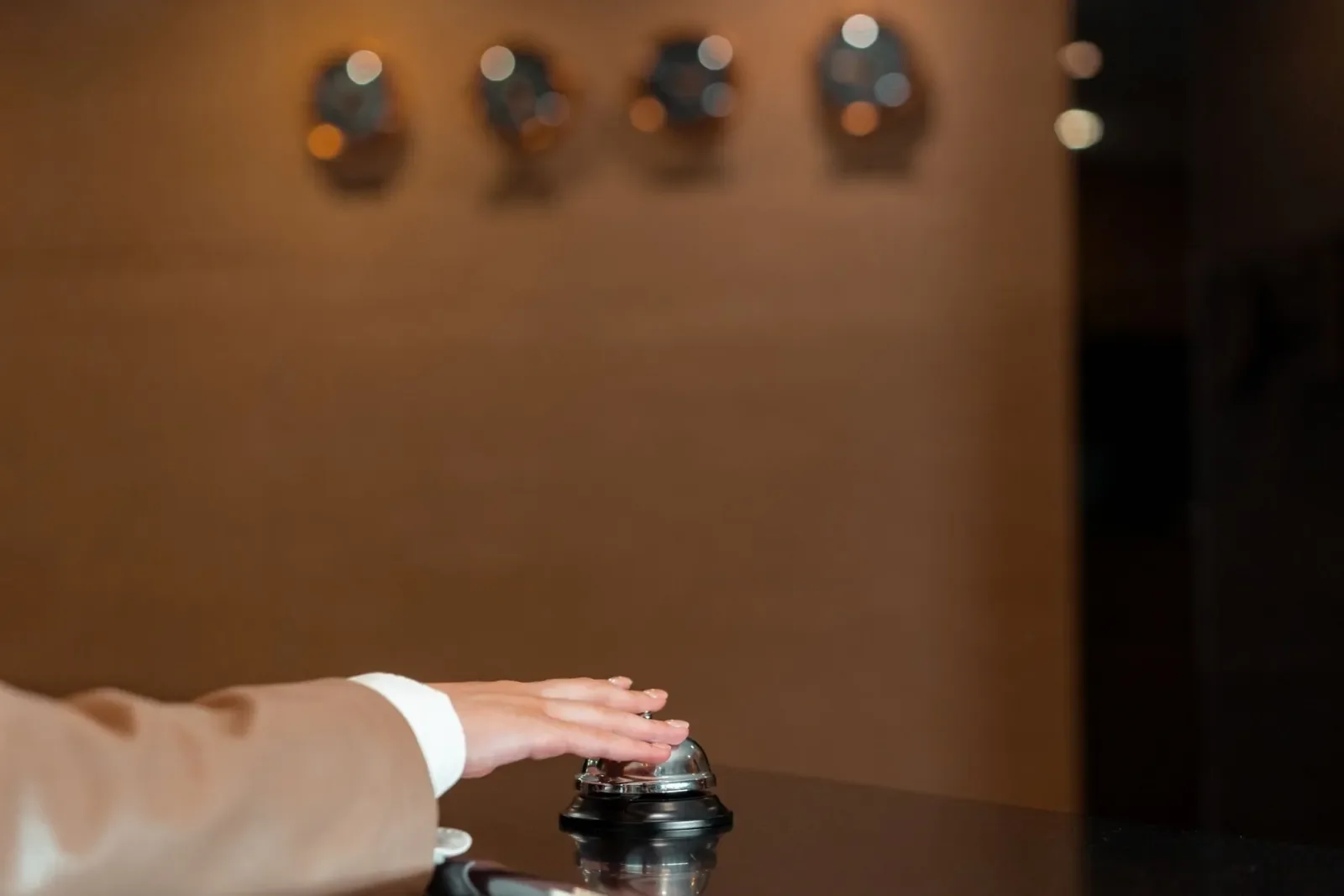 Una mano pulsa el timbre dorado de un mostrador de recepción